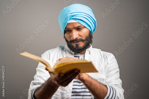 young sikh man reading holy religious Scripture for praying god on grey background - concept of spiritual belifes, worship and traditional culture. photo