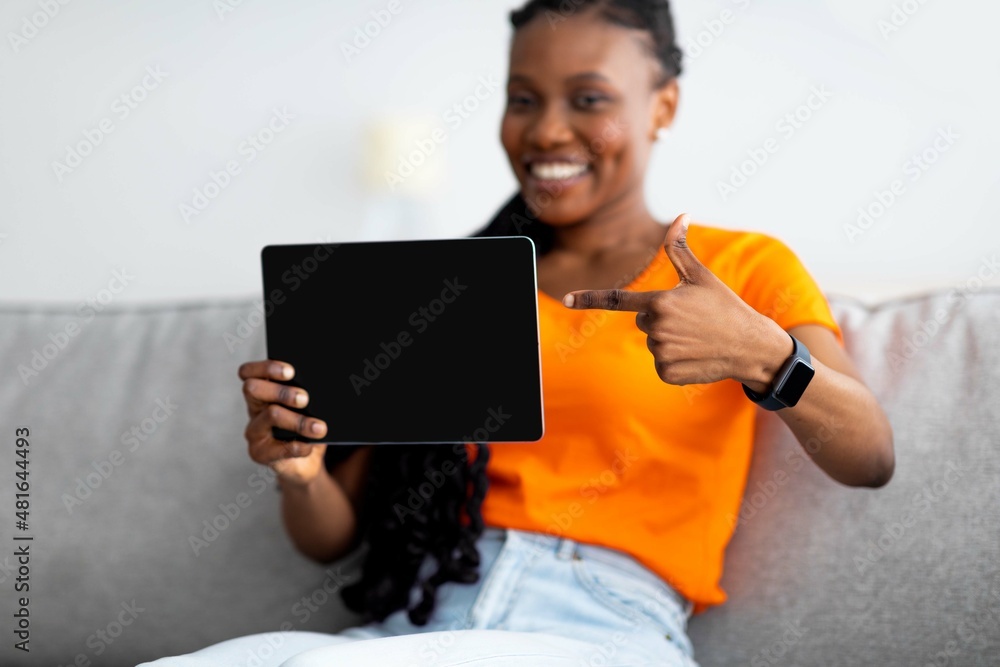 Internet purchases. Happy black woman pointing at tablet screen with mockup for shopping app or website design at home Internet purchases. Happy black woman pointing at tablet screen with mockup for shopping app or website design at home