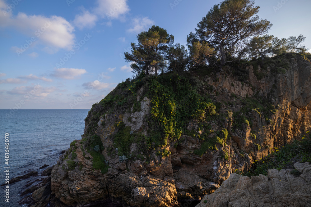 Seascape. Mediterranean evening. Rocks surrounded by water on the beach protruding into the sea on a sunny day, Blanes, Catalonia, Spain.