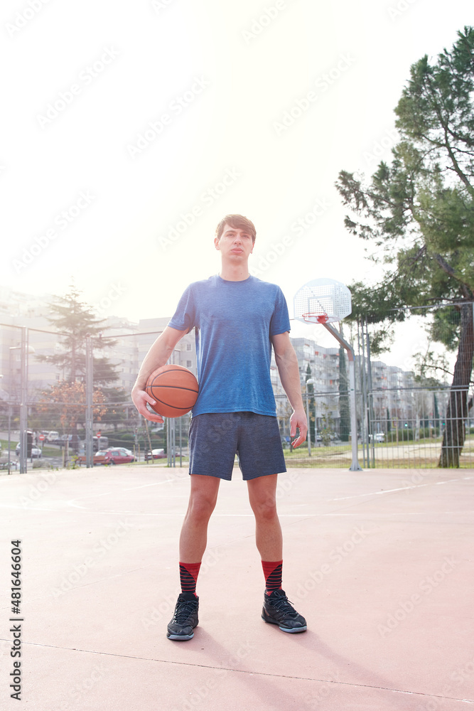 portrait of a young man on a basketball court. holding a basketball. vertical picture