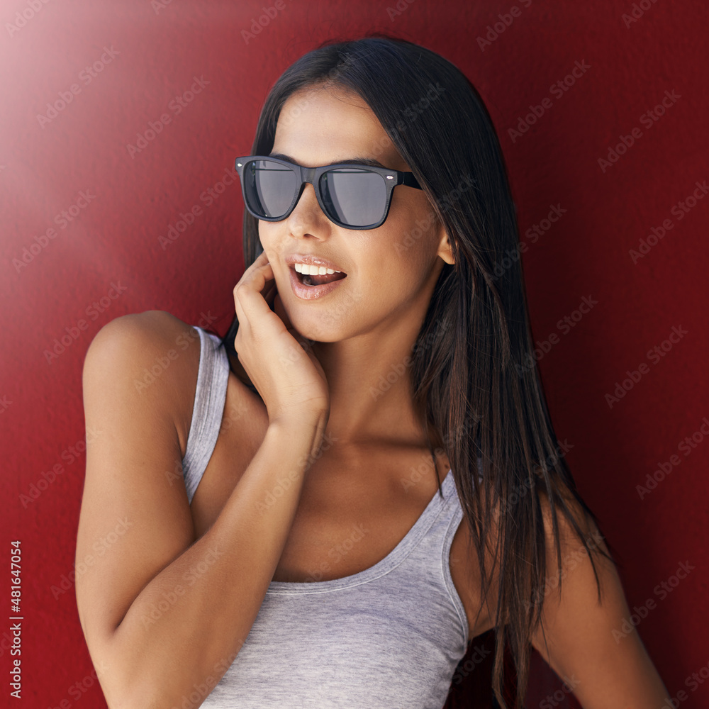 24/7 cool. Shot of an attractive young woman wearing sunglasses against a red background. 24/7 cool. Shot of an attractive young woman wearing sunglasses against a red background.