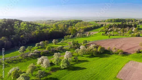 Scenic green landscape with meadows, hills and forests in spring, with cars driving on a road, shot from above and moving backwards
