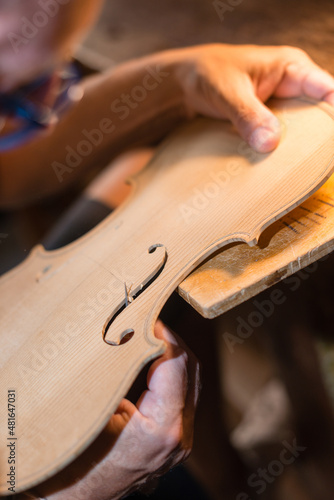 Fotografie Luthier making a handmade classic italian violin, working  and carving  the f-ho