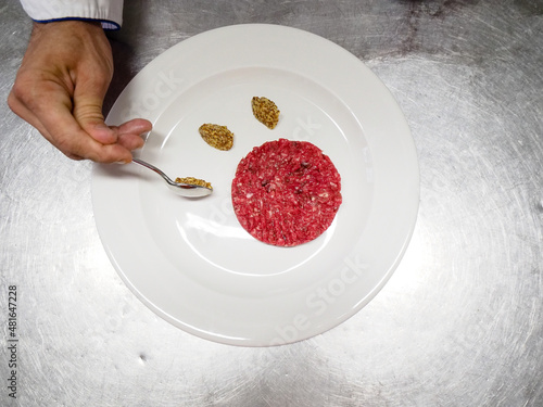 hand of chef  serving scottona raw meat tartare with moutard on a white dish in the kitchen of a restaurant photo