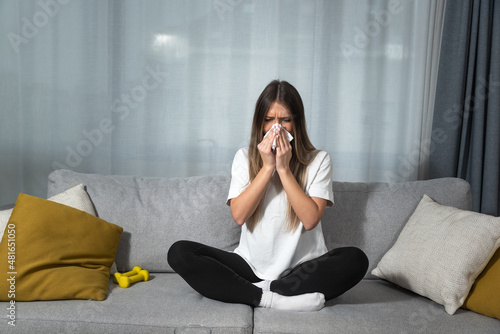 Young woman suffering from a common cold and flu or allergy sitting at home and wipe her nose with tissues while she have strong headache pain. Female with strong allergic reaction healthcare concept photo