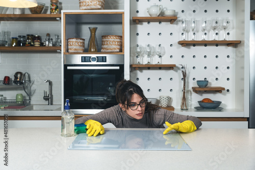 Young woman suffers from depression after a breakup or divorce and from obsessive compulsive disorder OCD cleans kitchen cook top to calm her nerves. Serious stressed female rubbing the home
