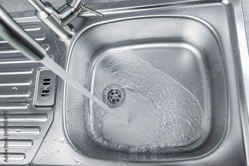 Wasser fliesst aus einem Wasserhan in ein Spülbecken