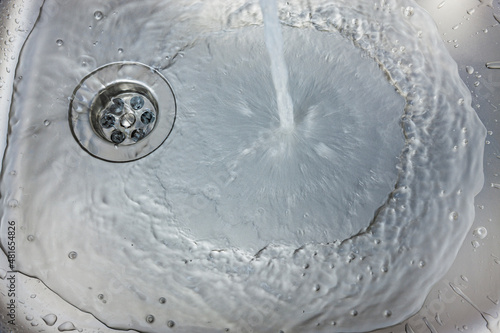 Wasser fliesst aus einem Wasserhan in ein Spülbecken