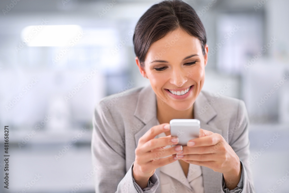 She's always available. Shot of a woman using a cellphone while sitting at a desk in an office.
