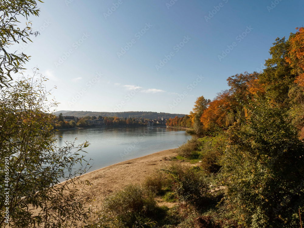 Rheinfelden (Baden). Bewaldetes Ufer in herbstlicher Farbgebung und kleiner Sandstrand auf deutscher Seite am Rheinufer gegenüber Rheinfelden (Aargau)