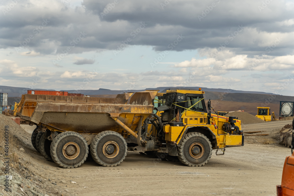 An articulated dump truck waiting to be repaired stands near the containers at the gold mine site. An articulated dump truck waiting to be repaired stands near the containers at the gold mine site.