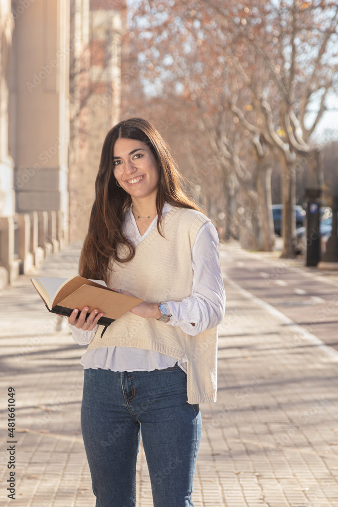 Fototapeta premium Student girl smiling while looking at camera. Young lady with a notebook in her hand on the university campus.