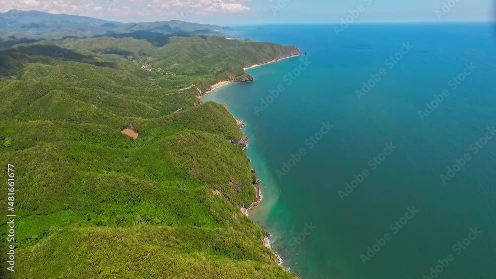 Aerial view of the  venezuelan caribbean sea in the morning near the coast with cliffs and  of evergreen forest, next to a tropical beach with palm trees and beige sand, under a clear sky with clouds
