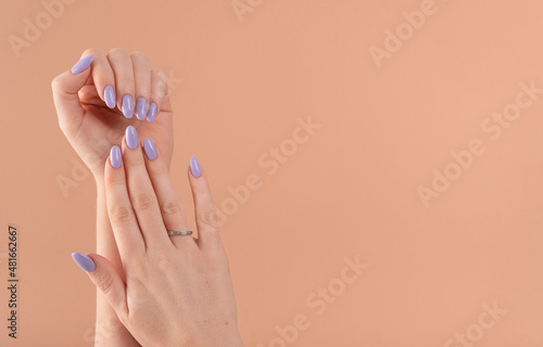 Hands of a beautiful well-groomed with feminine violet lavender nails gel polish on a beige background. Manicure, pedicure beauty salon concept.