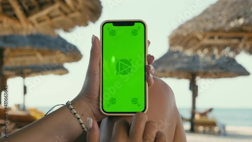 Mockup of a Young Woman Holding Phone with Green Screen Laying on a Sun Lounger on the Beach. Mobile Smartphone App Commercial Concept. X2 Slow Motion