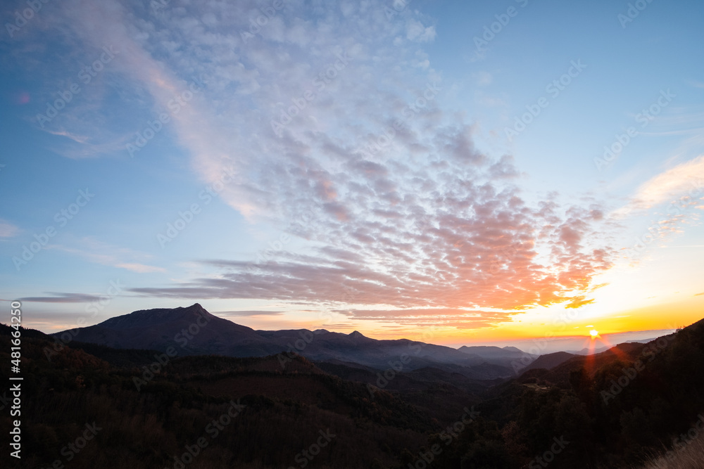 Sun rising and shining on the horizon of a beautiful landscape with some cirrus in the high sky