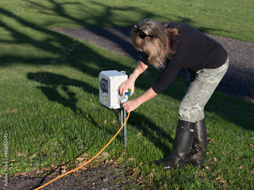 Photos A female motorhomer plugs the orange electric hook up lead into a campsite supply point using the blue connector