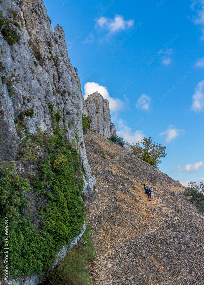 Hikers ascending a mountain in a sunny day under a beautiful cloudy sky.