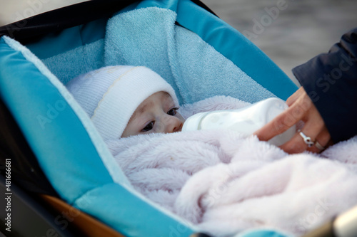Un bébé boit à son biberon dans sa poussette bleue