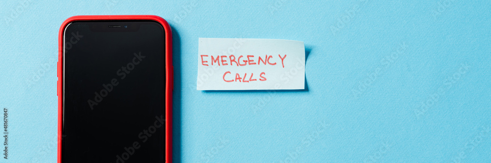 Overhead view of the phone with the turning screen to the camera, lying with a piece of paper emergency calls in a studio Overhead view of the phone with the turning screen to the camera, lying with a piece of paper emergency calls in a studio