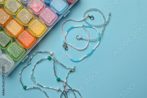 Beautiful handmade beaded jewelry and supplies on light blue background, flat lay