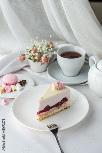 Delicious cherry mousse cake slice with the layers and cup of tea on the table