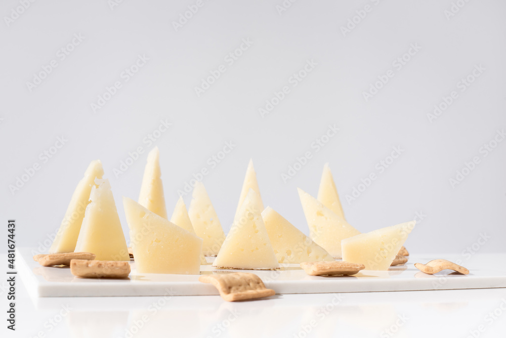 Trozos de queso manchego de oveja curado con tostadas de pan crujiente sobre una mesa blanca. Tapas españolas Trozos de queso manchego de oveja curado con tostadas de pan crujiente sobre una mesa blanca. Tapas españolas