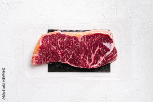 Raw marbled beef steaks in vacuum pack, on white stone table background, top view flat lay, with copy space for text