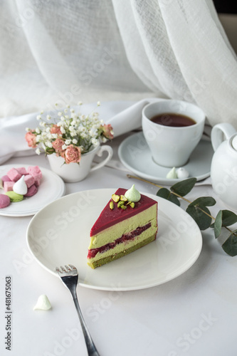 Slice of pistachio mousse cake with raspberry and cup of tea on the table