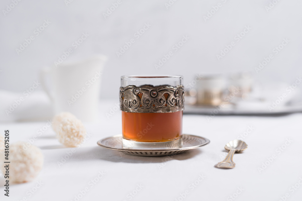 Un vaso de té clásico con dulces chocolates blancos cubiertos de coco en el cuadro blanco Un vaso de té clásico con dulces chocolates blancos cubiertos de coco en el cuadro blanco