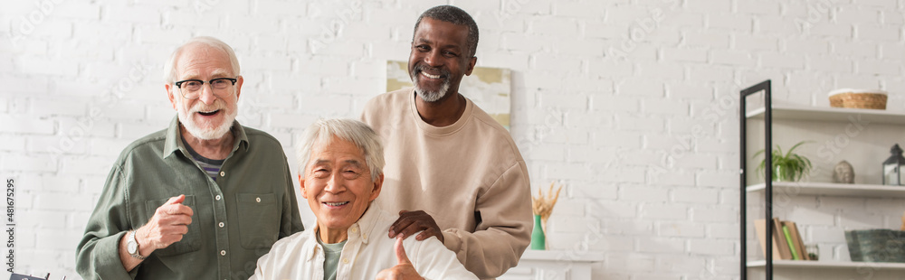 Smiling asian man showing like gesture near multiethnic friends at home, banner. Smiling asian man showing like gesture near multiethnic friends at home, banner.