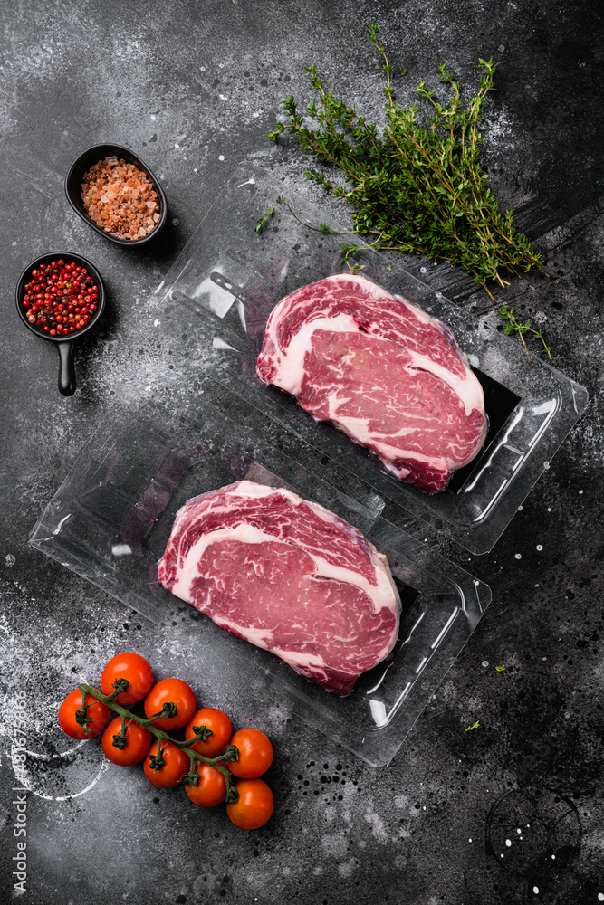 Rib-eye beef steak in plastic packing tray, on black dark stone table background, top view flat lay