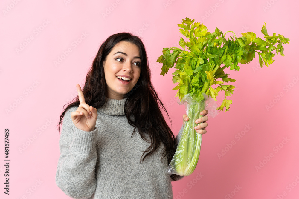 Young caucasian woman holding a celery isolated on blue background intending to realizes the solution while lifting a finger up Young caucasian woman holding a celery isolated on blue background intending to realizes the solution while lifting a finger up