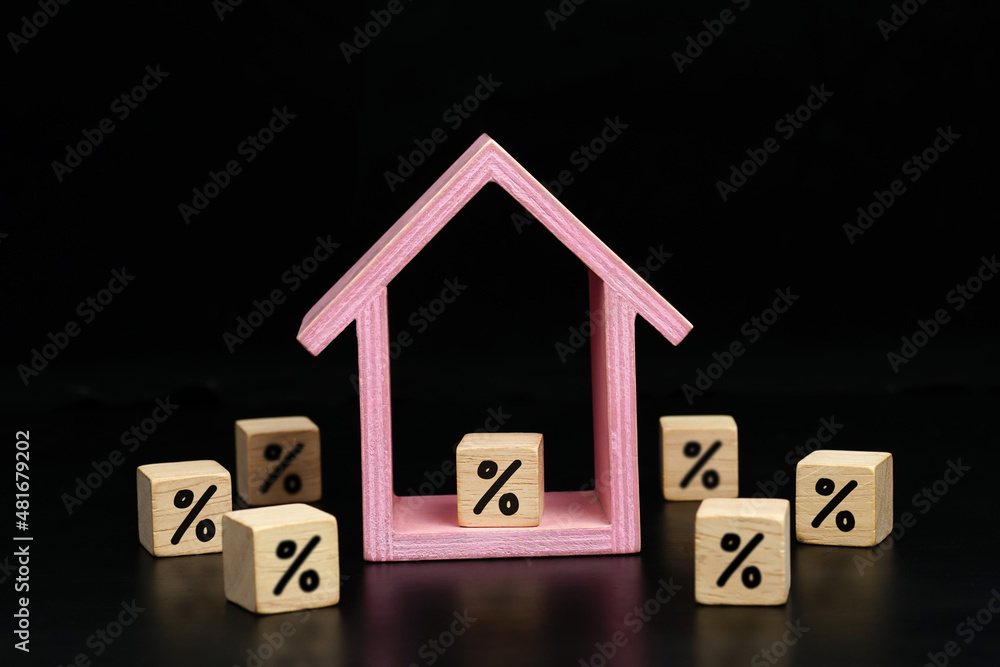 percent symbol icon on wood block and wooden house on a dark background. real estate interest concept. percent symbol icon on wood block and wooden house on a dark background. real estate interest concept.