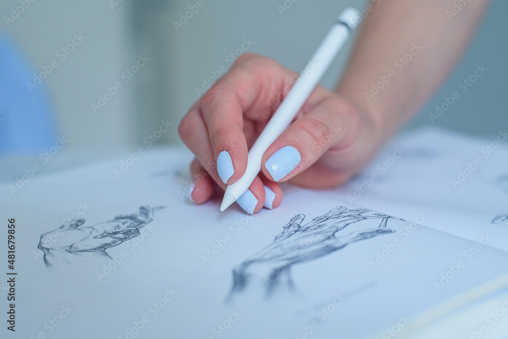 Woman holding digital pen and pointing at pencil sketches in the book.