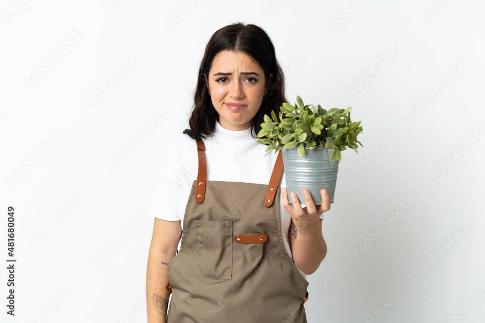 Young caucasian woman holding a plant isolated on white background with sad expression Young caucasian woman holding a plant isolated on white background with sad expression