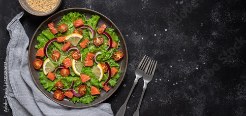 Salad with salmon and fresh vegetables on a black concrete background. Top view, flat lay, copy space. Banner.