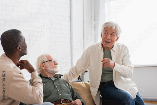 Elderly asian man talking to multiethnic friends in living room.