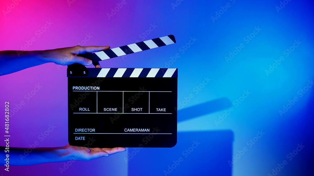 Blurry images of movie slate or clapper board. Hand holds empty film making clapperboard on color background in studio for film movie shooting or recording. Film slate for Youtuber video production. - obrazy, fototapety, plakaty 