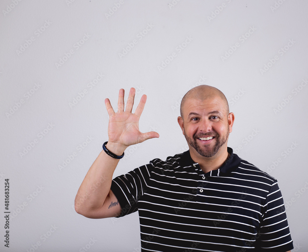 Naklejka premium Hispanic bald man standing in front of a white background and making emotional gestures holding up 5 fingers 