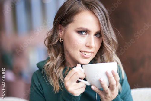 Close-up portrait of an optimistic beautiful woman with a beautiful manicure  holding a cup  sitting in a cafe  the girl looks directly into the camera. High quality photo