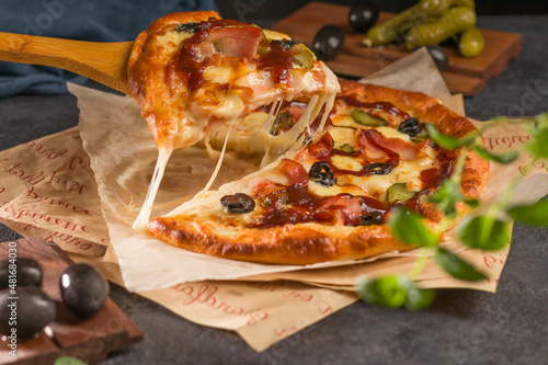 Wallpaper Mural Closeup pizza with bacon, basil, olives, pickles and mozzarella cheese on parchment paper on a dark background. Delicious fresh and homemade fast food. Torontodigital.ca