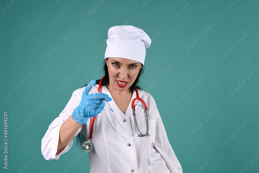 A female doctor in a white coat and a white headdress with a vaccine syringe on a green background with a stethoscope in a threatening pose. The doctor has gone mad A female doctor in a white coat and a white headdress with a vaccine syringe on a green background with a stethoscope in a threatening pose. The doctor has gone mad