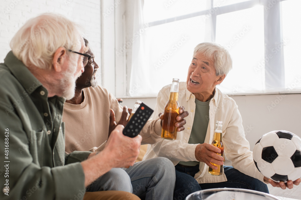 Asian man holding football near interracial friends with beer at home. Asian man holding football near interracial friends with beer at home.