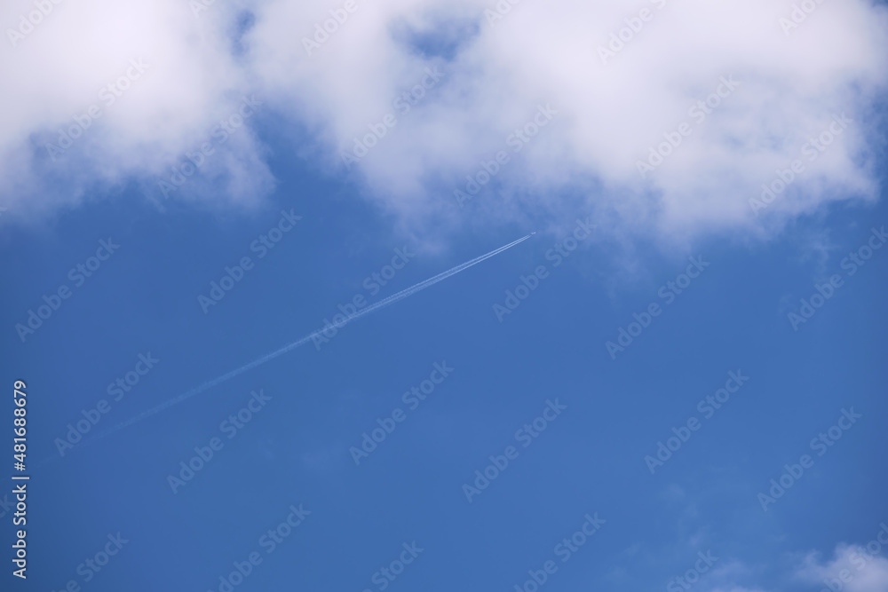Distant passenger jet plane flying on high altitude on blue sky with white clouds leaving smoke trace of contrail behind. Air traveling concept Distant passenger jet plane flying on high altitude on blue sky with white clouds leaving smoke trace of contrail behind. Air traveling concept