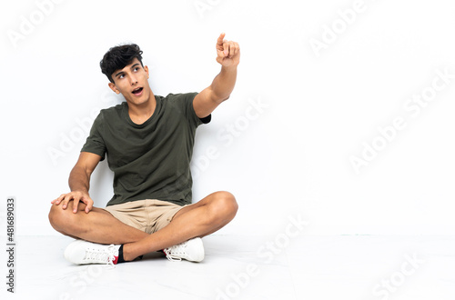 Young Argentinian man sitting on the floor pointing away