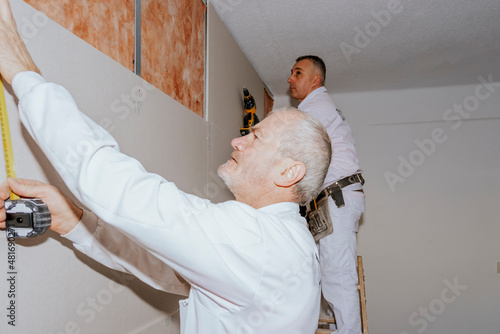 Two workers installing plasterboard panels with acoustic insulation. photo