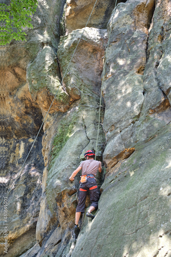 Young man climbing steep wall of rocky mountain. Male climber overcomes challenging route. Engaging in extreme sport concept Young man climbing steep wall of rocky mountain. Male climber overcomes challenging route. Engaging in extreme sport concept