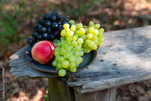 Black and green grapes and nectarine on a tray. Fresh summer fruits on the old wooden bench.