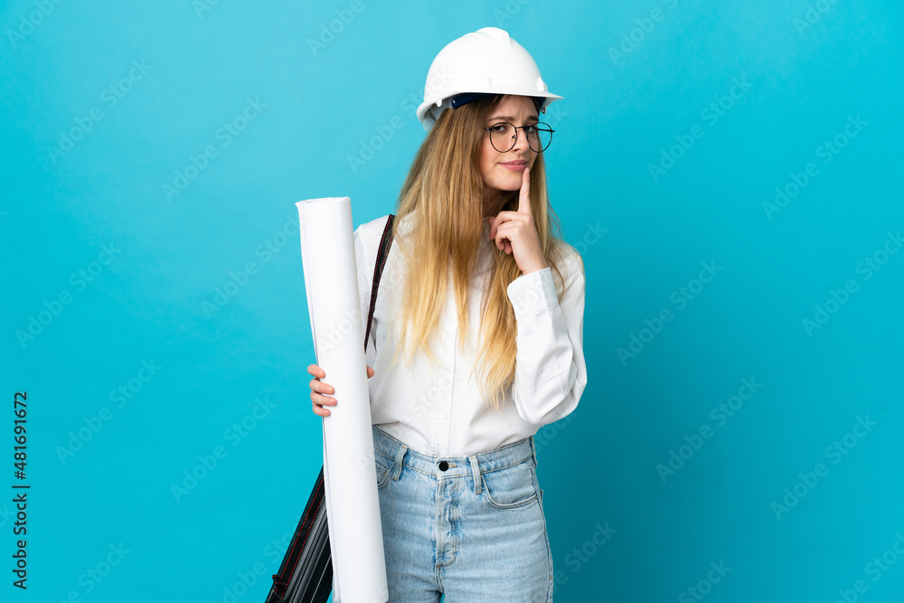Young architect woman with helmet and holding blueprints isolated on blue background having doubts while looking up Young architect woman with helmet and holding blueprints isolated on blue background having doubts while looking up